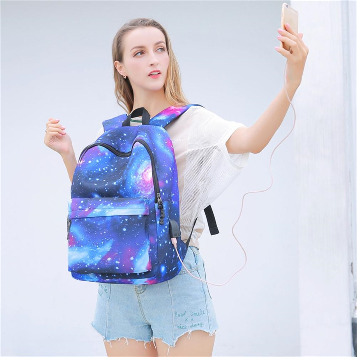 Eine Frau macht ein Selfie mit einem Rucksack im Galaxie-Design und einem Ladekabel.