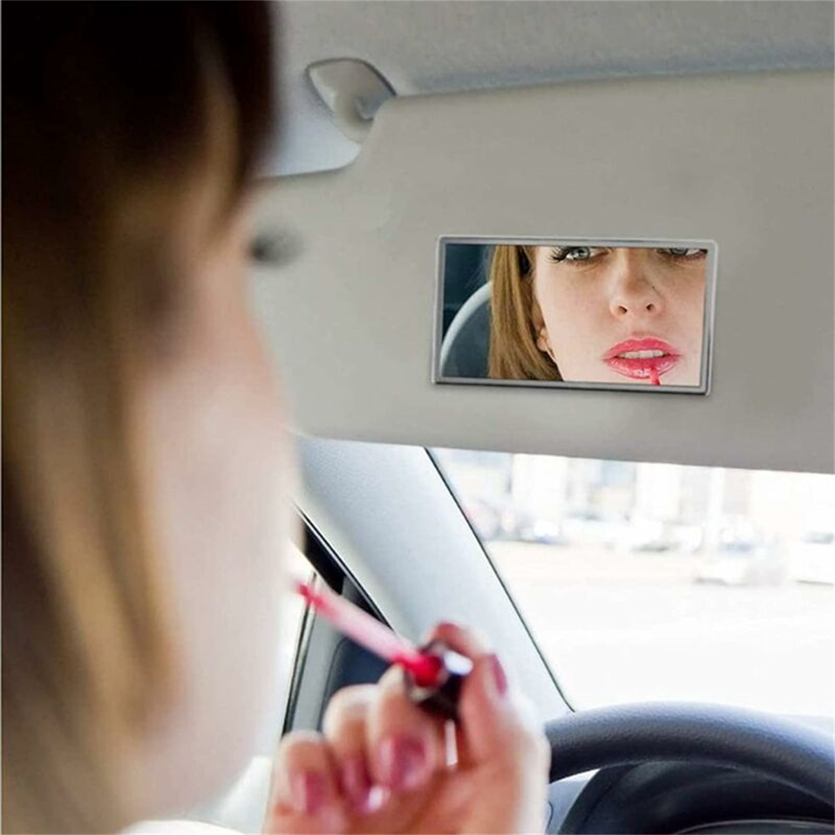 Frau, die roten Lippenstift in einem Autospiegel aufträgt, verschwommener Hintergrund sichtbar.