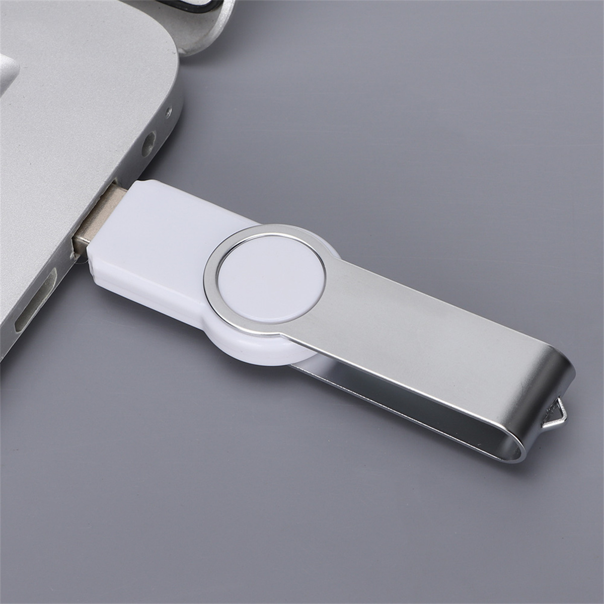 Weißer USB-Stick in einen Laptop gesteckt, auf grauer Oberfläche, mit silbernem Rand.