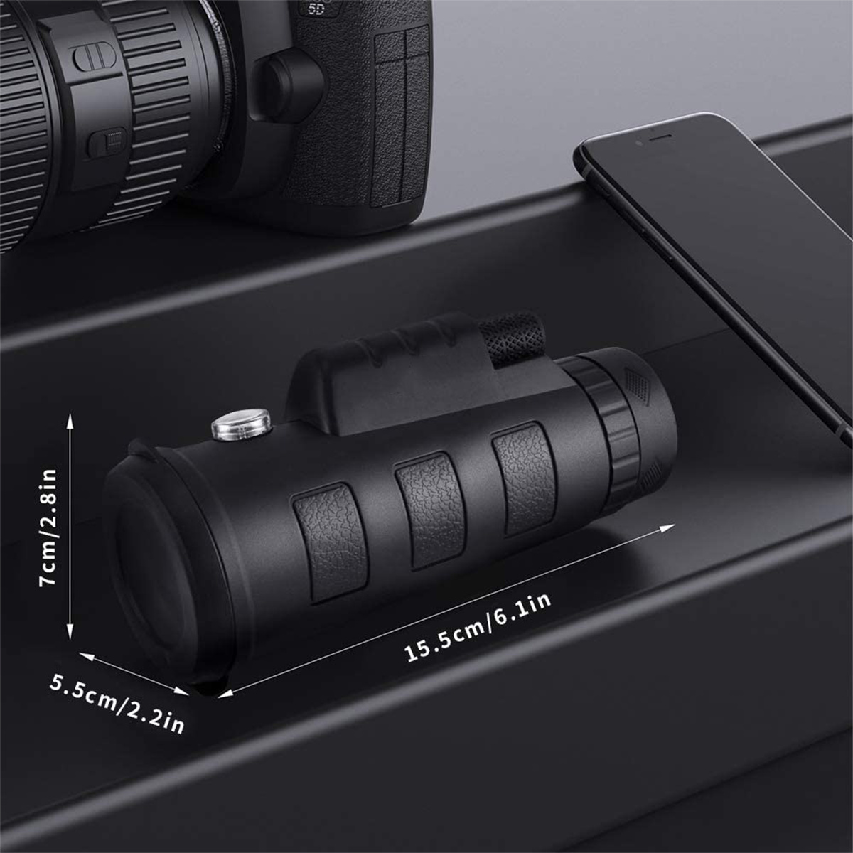 Schwarzes Monokular, 7cm hoch, 5,5cm breit und 15,5cm lang. Telefon und Kamera im Hintergrund.