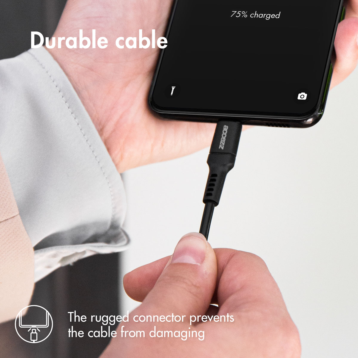 Main tenant un câble de charge noir connecté à un téléphone, chargé à 75%.