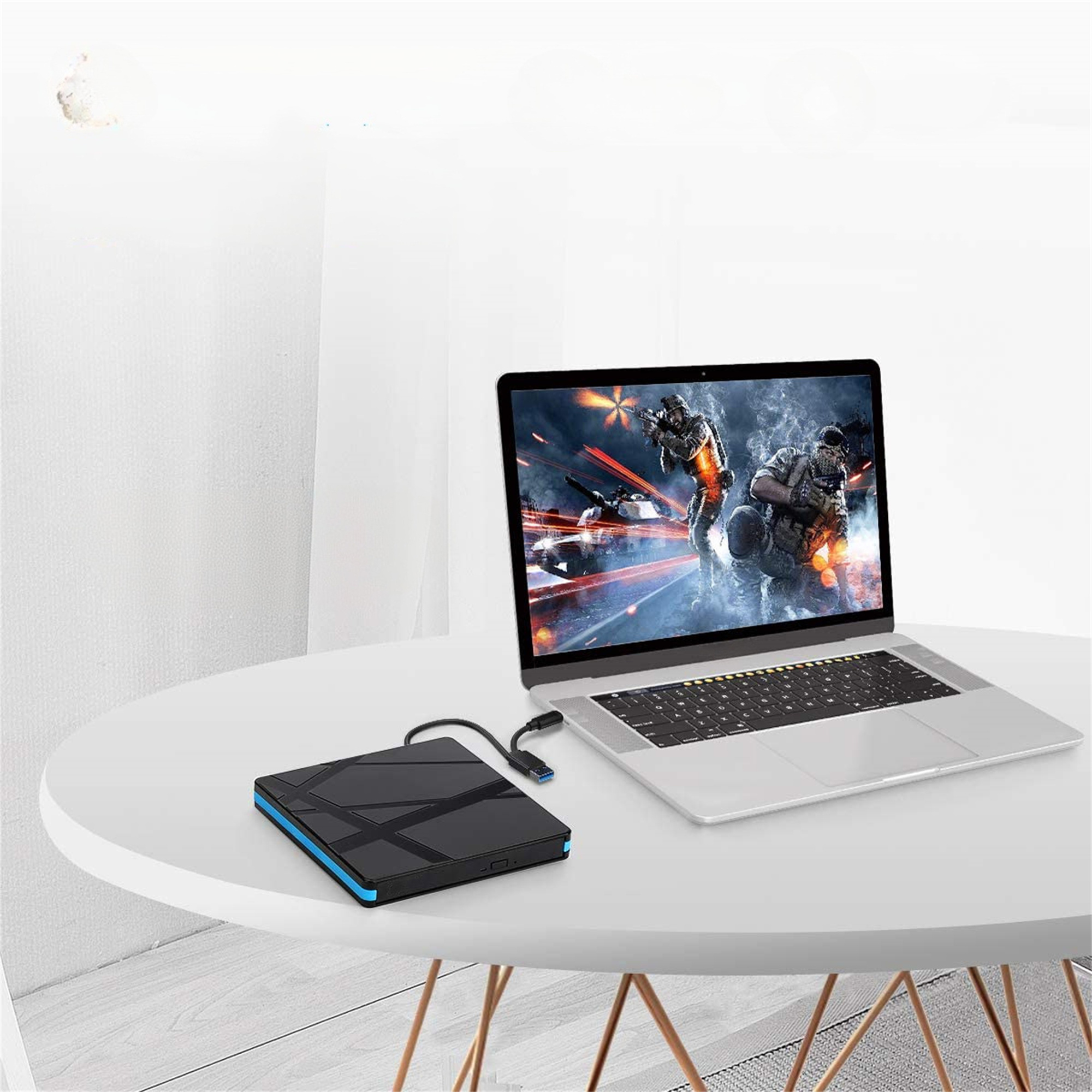 Laptop mit Spiel, mit schwarzer externer Festplatte und Kabel auf weißem Tisch.