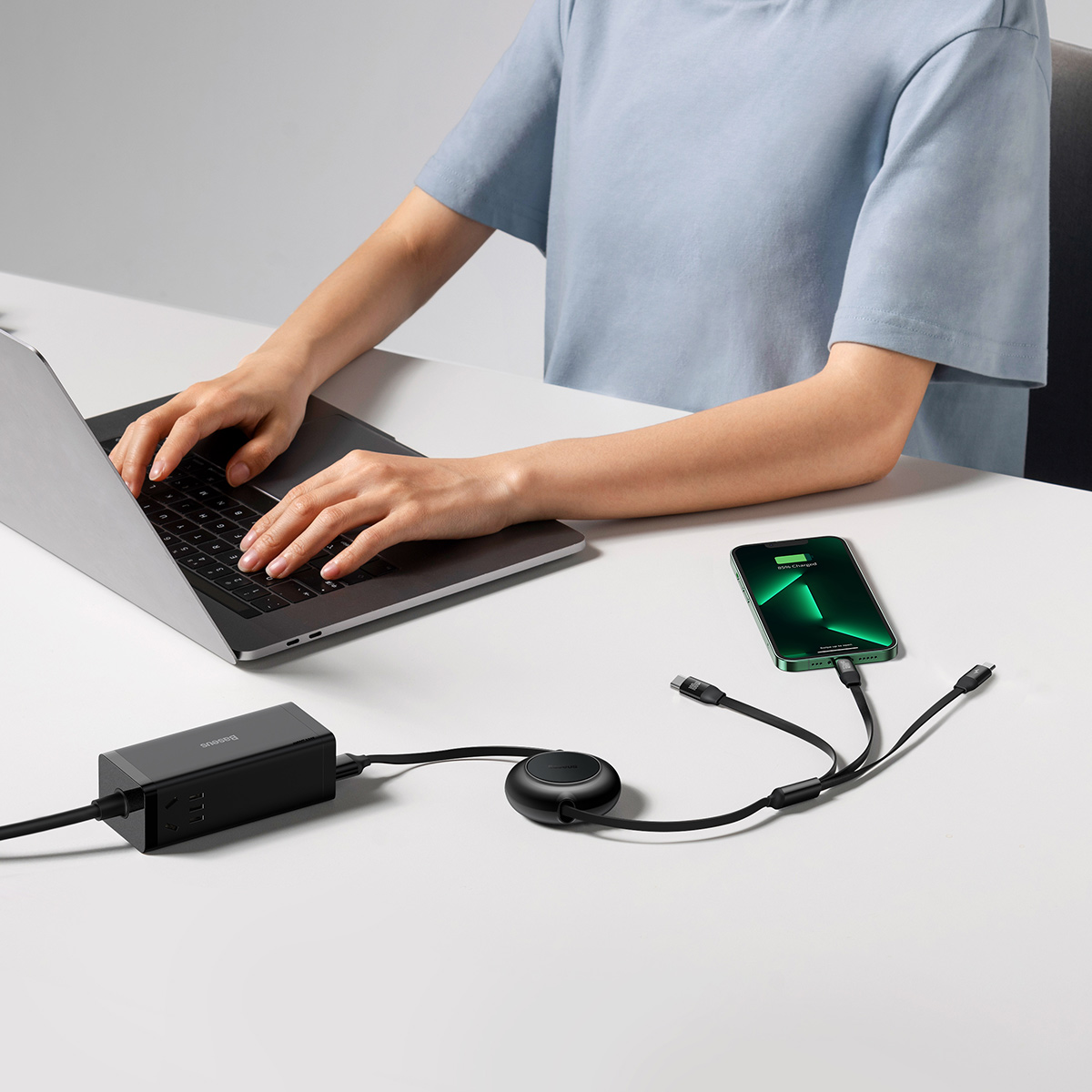 Person using laptop with phone and charger on desk.