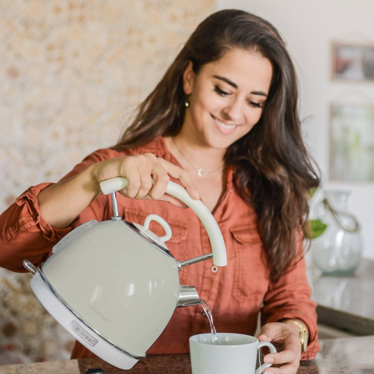 Frau gießt Wasser aus einem Kessel im Vintage-Stil in eine Tasse.