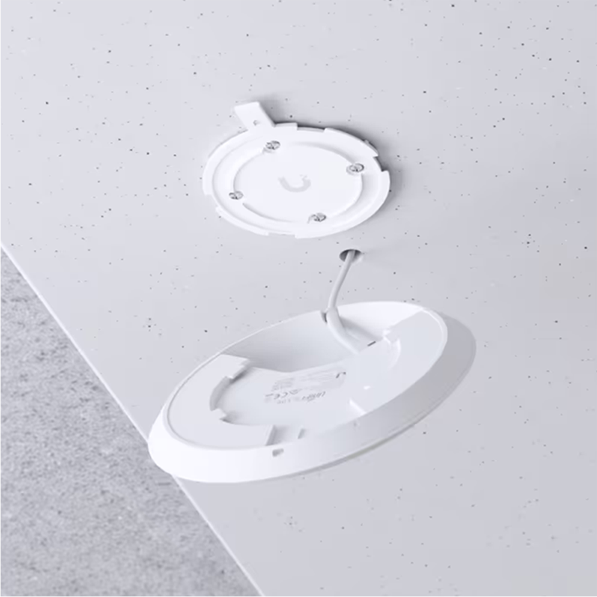 Witte plafondbevestiging met een cirkelvormig ontwerp. Een deel is los, toont een kabel.