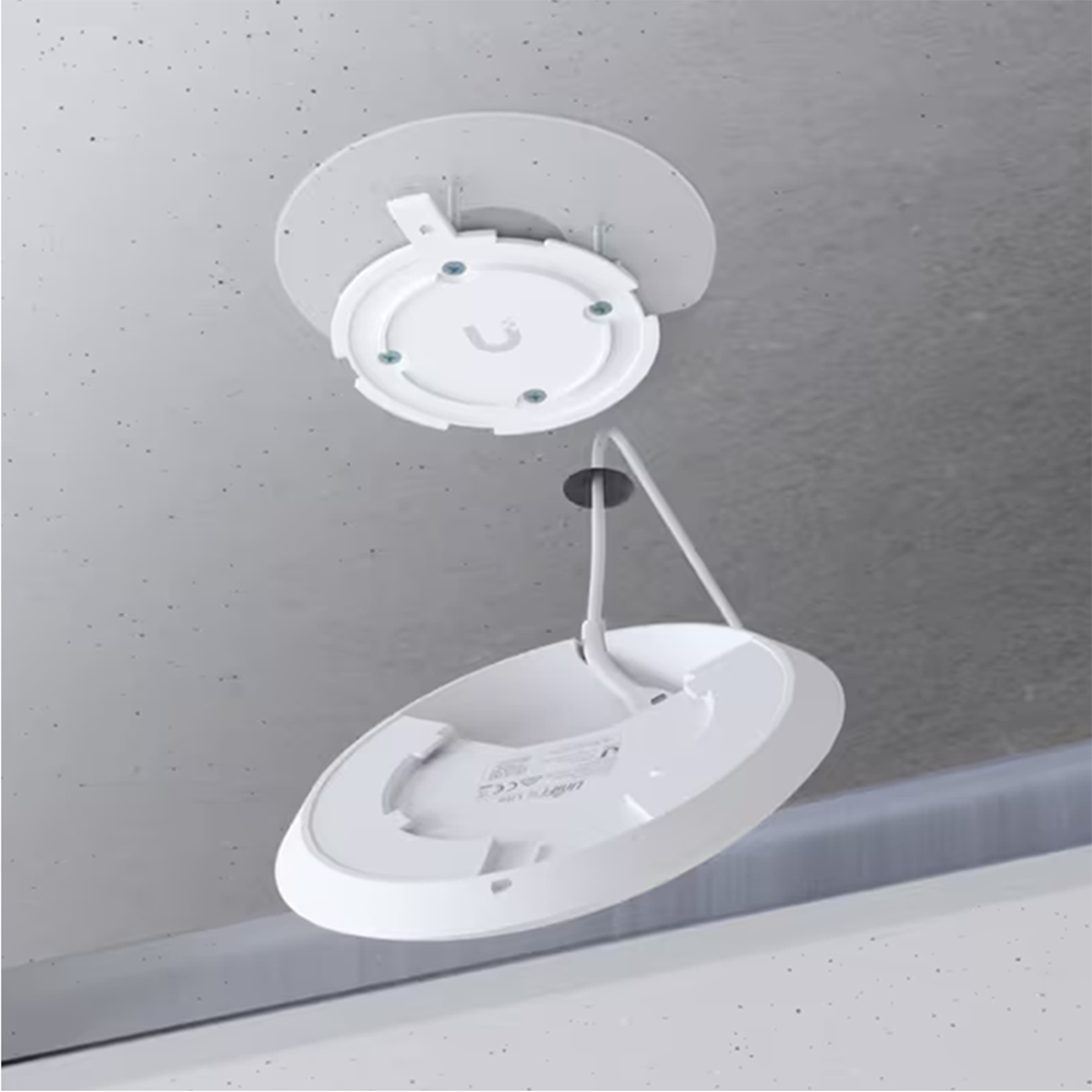 Een wit cirkelvormig apparaat wordt geïnstalleerd op een wit plafond. Een kabel hangt naar beneden.