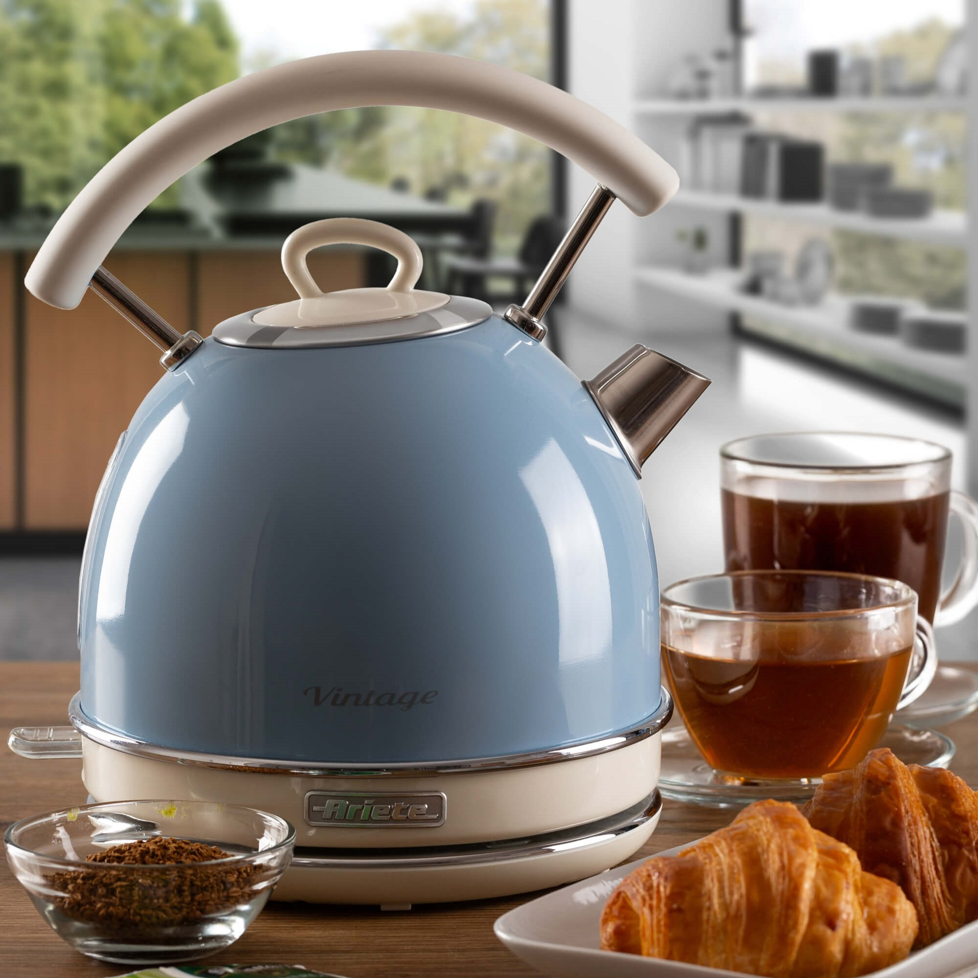 Blauwe vintage elektrische waterkoker met een witte handgreep, met twee kopjes thee en croissants.