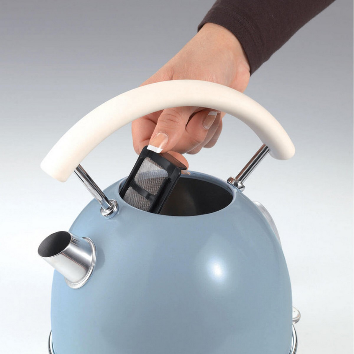 Hand plaatst filter in lichtblauwe waterkoker met witte handgreep en metalen voet.