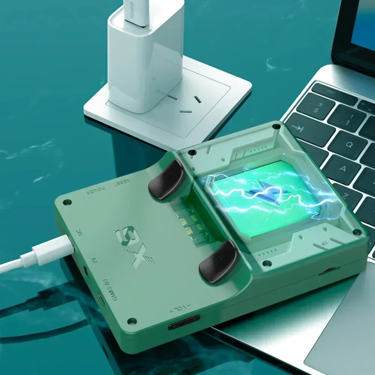 Consola de juegos portátil verde con pantalla, un ordenador portátil y cable de carga.