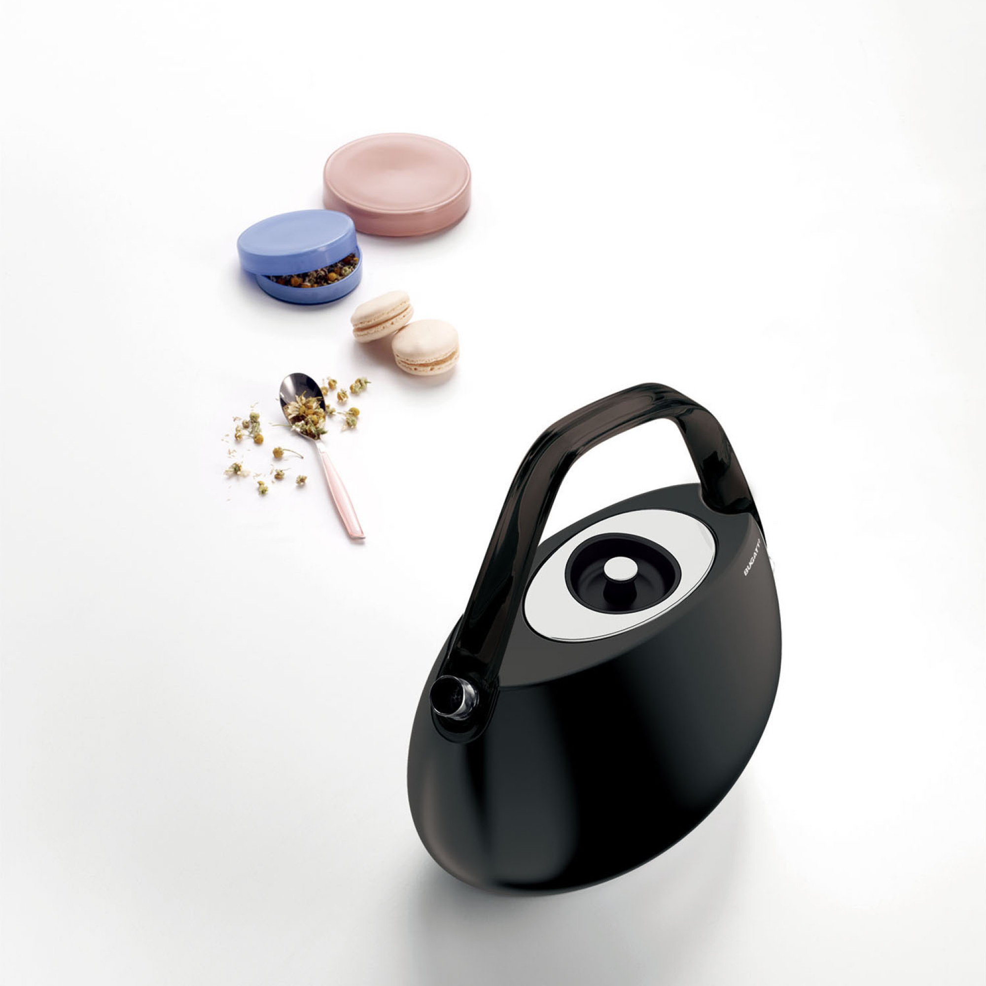 Un bollitore elettrico nero con decorazioni. Cucchiaini, macarons e tè su bianco.