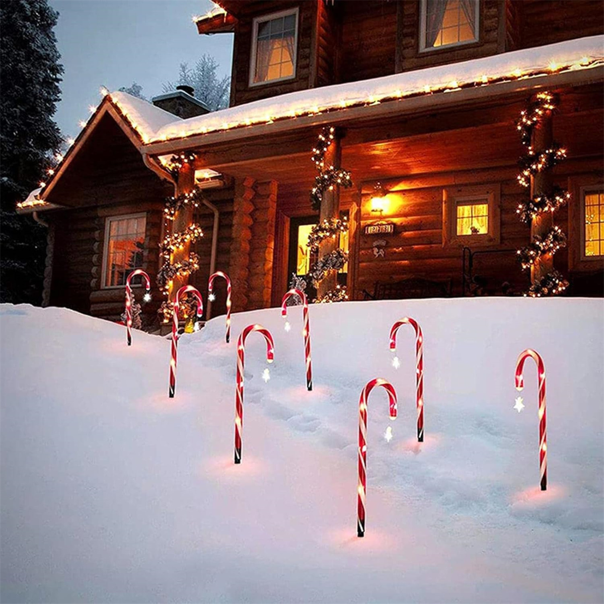 Weihnachts-Zuckerstangenlichter im Schnee. Haus im Hintergrund mit Lichtern auf dem Dach.