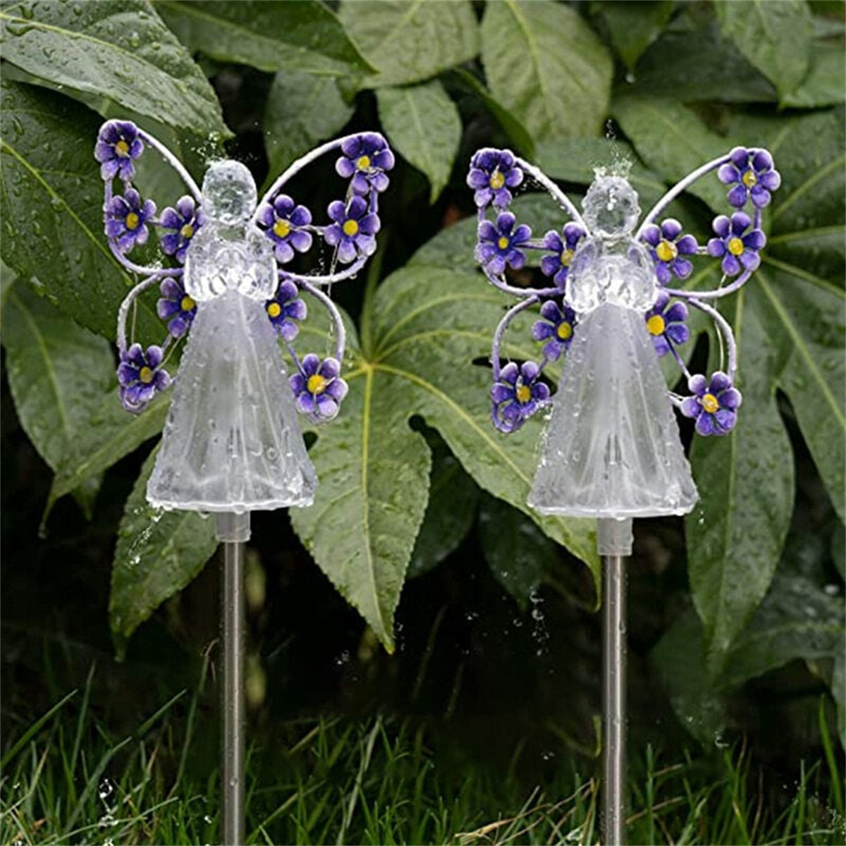 Zwei feenartige Gartenzierfiguren vor grünem Laub. Sie bestehen aus klarem Material.