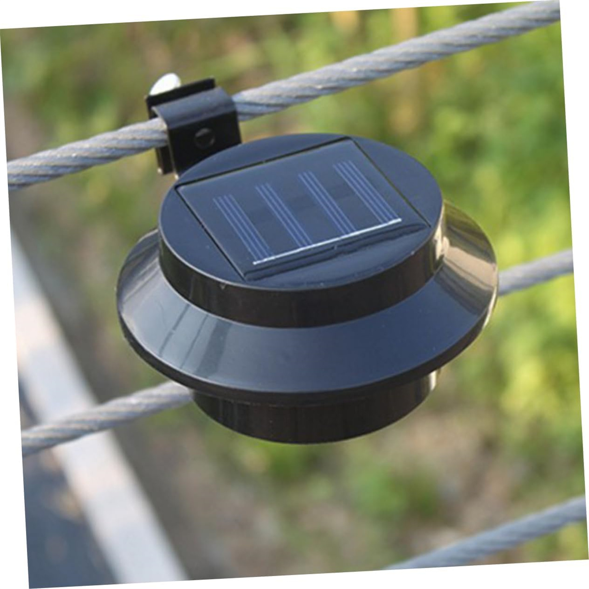Eine schwarze Solarpanel-Leuchte, die mit einer Klammer an einem Draht befestigt ist. Das Licht ist rund.