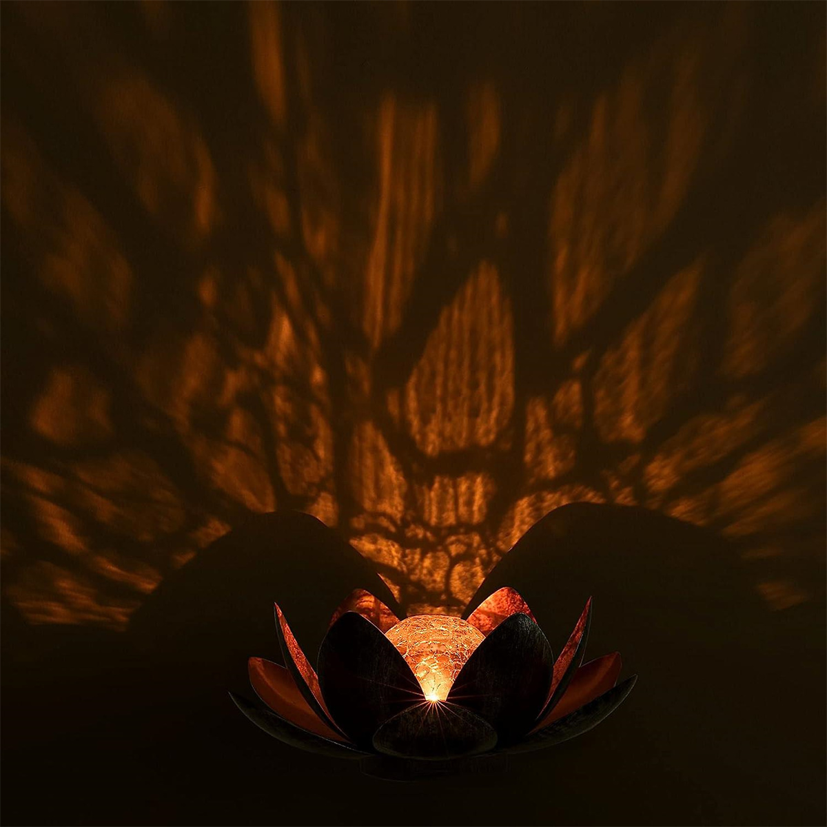 Lotusförmige Lampe, die leuchtet und Schatten von Ästen auf dunklem Hintergrund wirft.