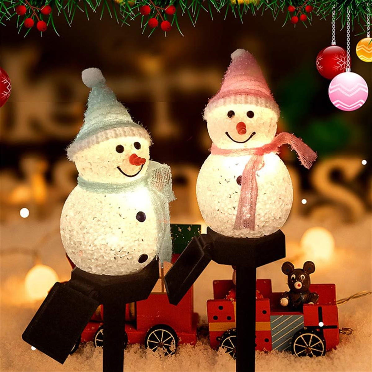 Zwei Schneemann-Dekorationen mit Hüten, Schals und Kohleaugen, auf verschwommenem Hintergrund mit Weihnachtsbeleuchtung.