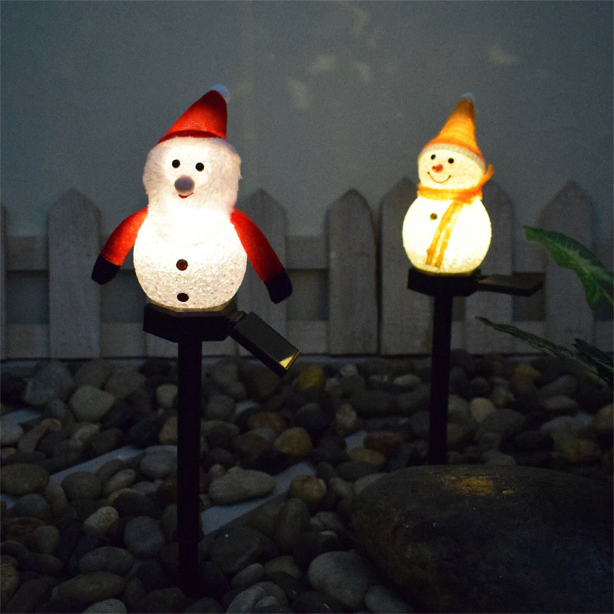 Zwei beleuchtete Schneemannfiguren auf Pfählen, in einem Garten.