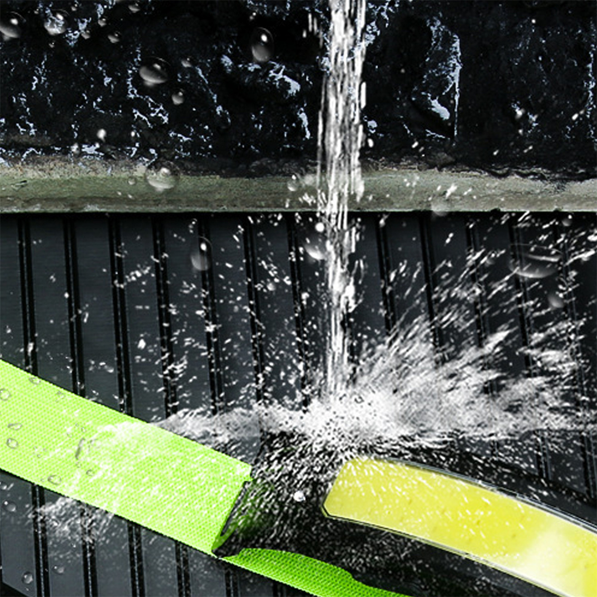 Wasser gießt auf einen grünen Riemen auf schwarzer Oberfläche, erzeugt Spritzer.