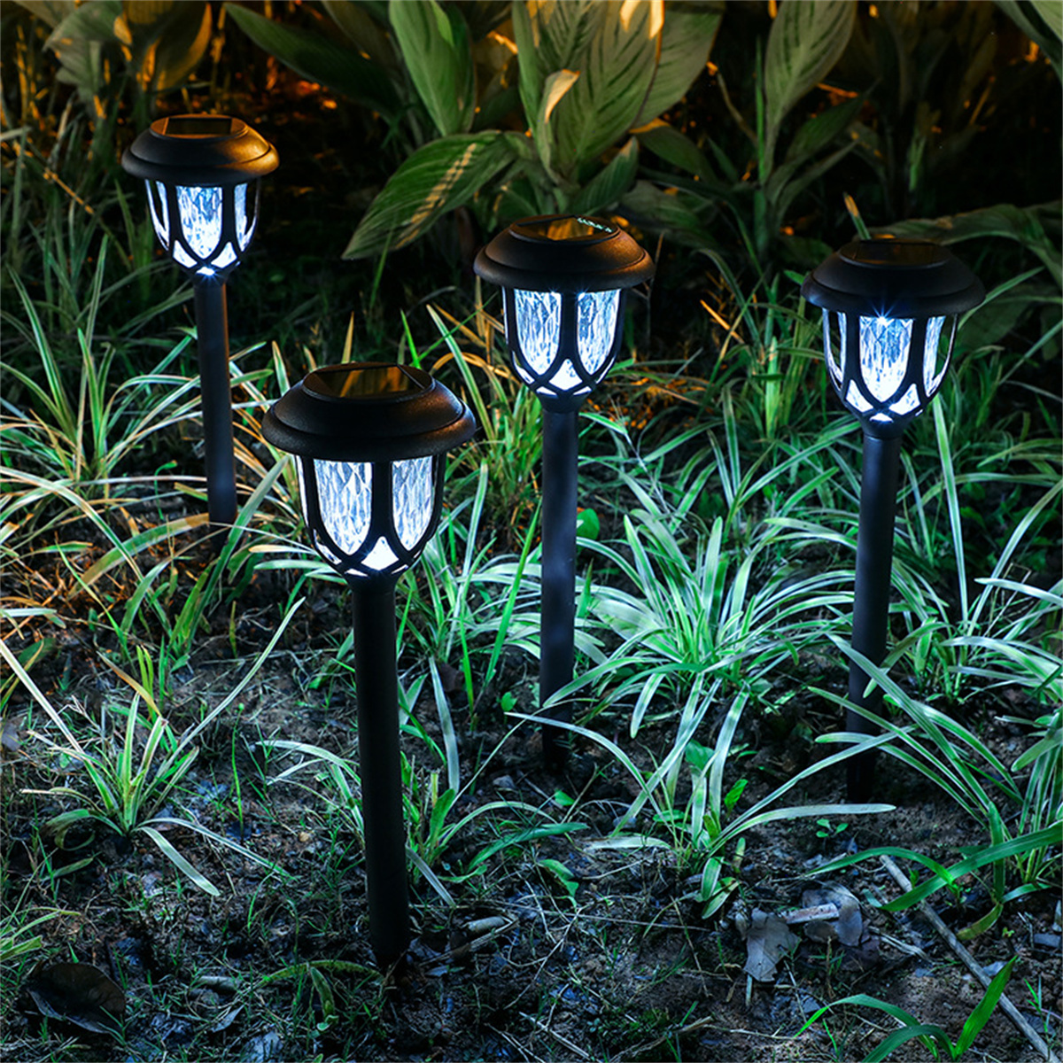 Vier Solar-Gartenleuchten mit schwarzem Pfahl im Boden. Die Lichter haben einen weißen Schein.