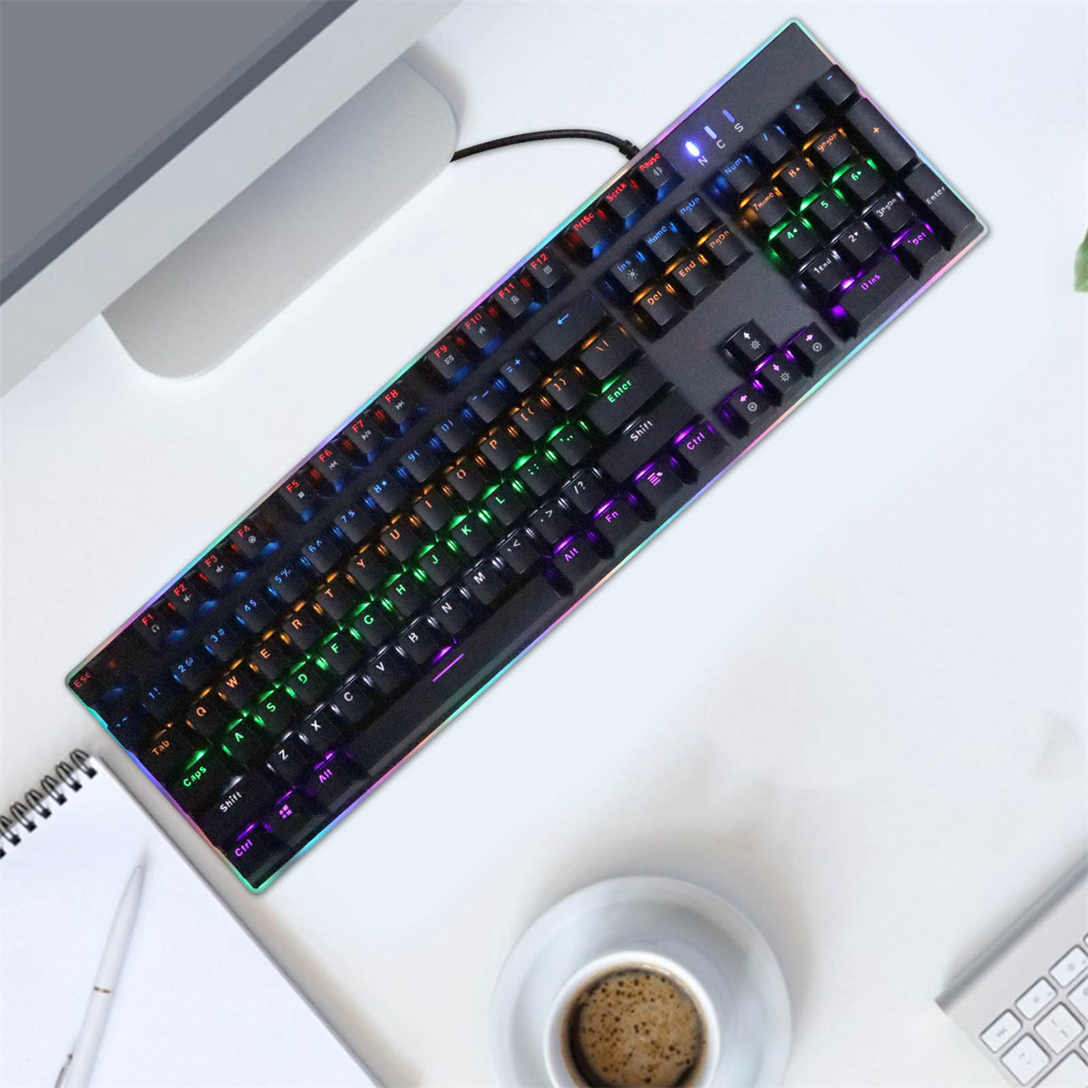 Schwarze Tastatur mit bunten Tasten auf weißer Oberfläche. Monitor und Kaffeetasse sind teilweise sichtbar.