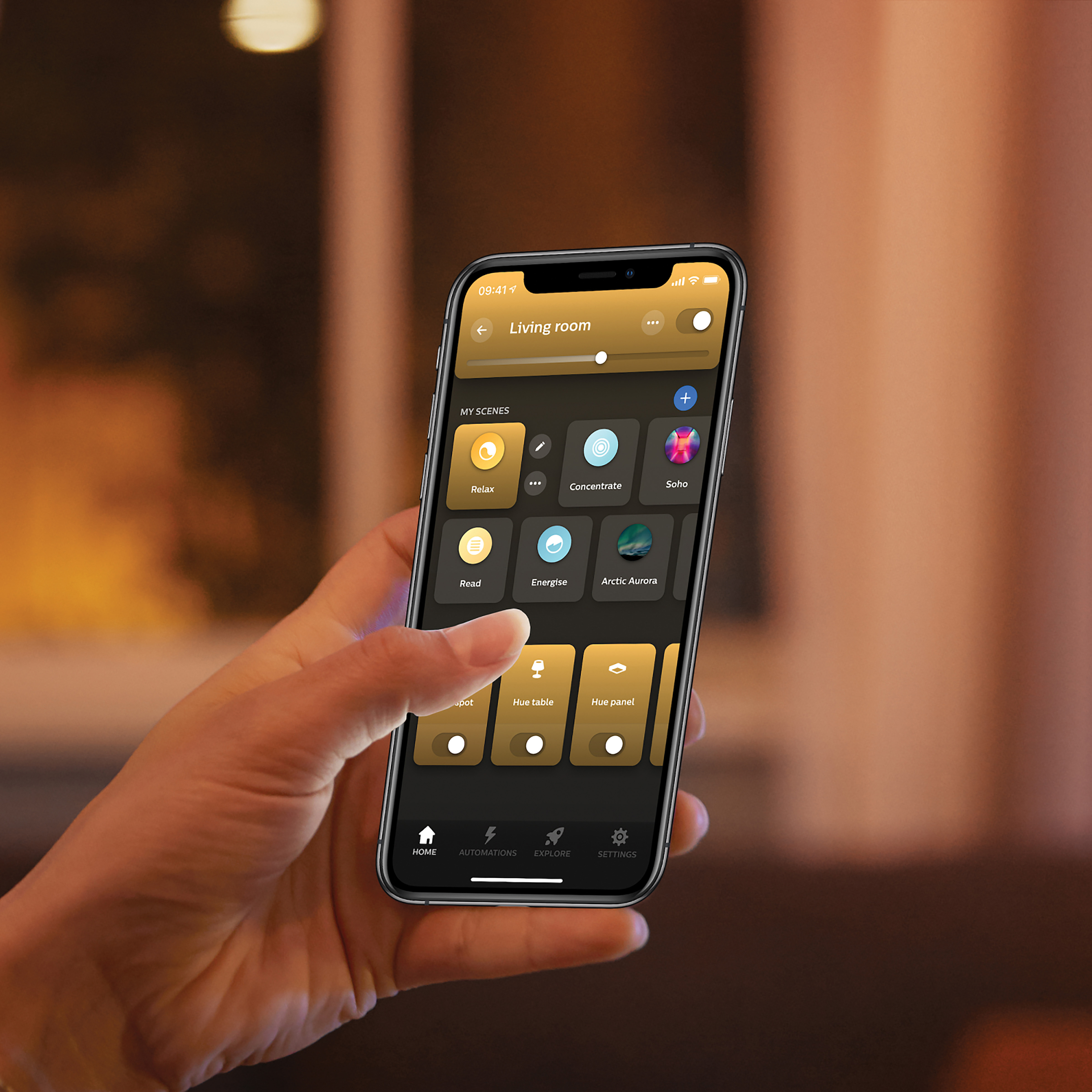 Dłoń trzymająca smartfon pokazujący aplikację do sterowania inteligentnym domem 'Living room' z różnymi opcjami oświetlenia.