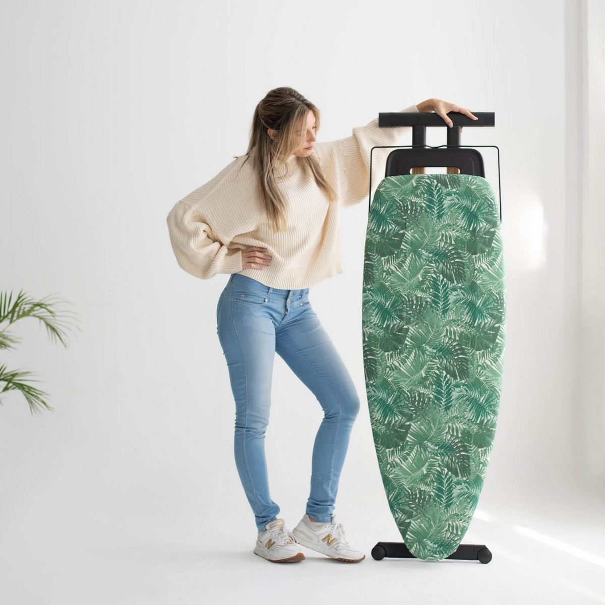 Una mujer está de pie cerca de una tabla de planchar con estampado de hojas verdes.