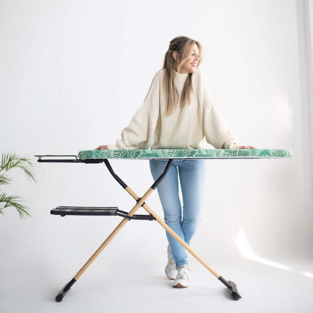 Una mujer sonríe apoyada en una tabla de planchar con estampado verde.