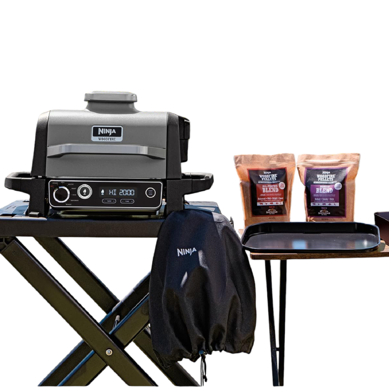 Grill Ninja Woodfire na czarnym stole, dwie torby z pelletem, osłona i taca, wszystko na białym tle.