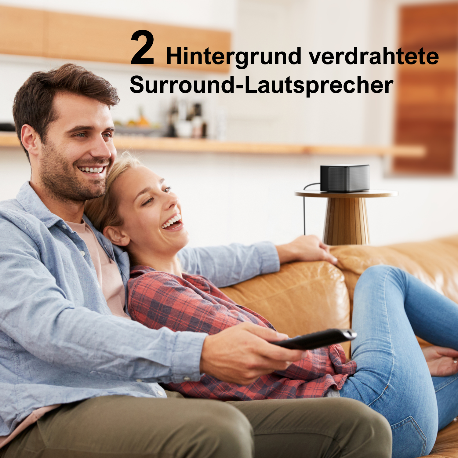 Ein Paar auf einer Couch schaut fern mit einem kleinen Lautsprecher auf einem Tisch in der Nähe.