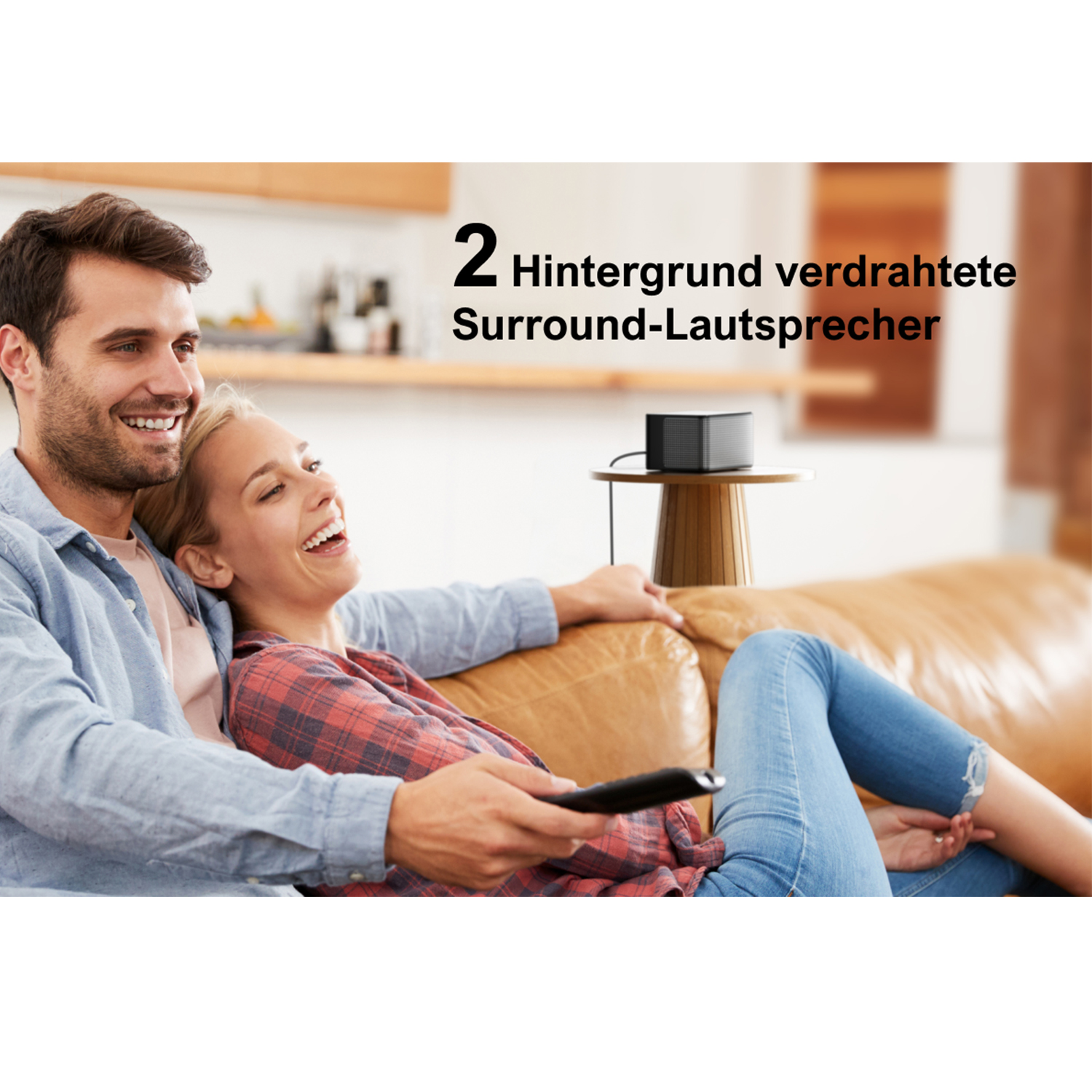 Ein Paar sitzt auf einem Sofa, lächelt und schaut fern. Ein kleiner schwarzer Lautsprecher steht auf einem Tisch.