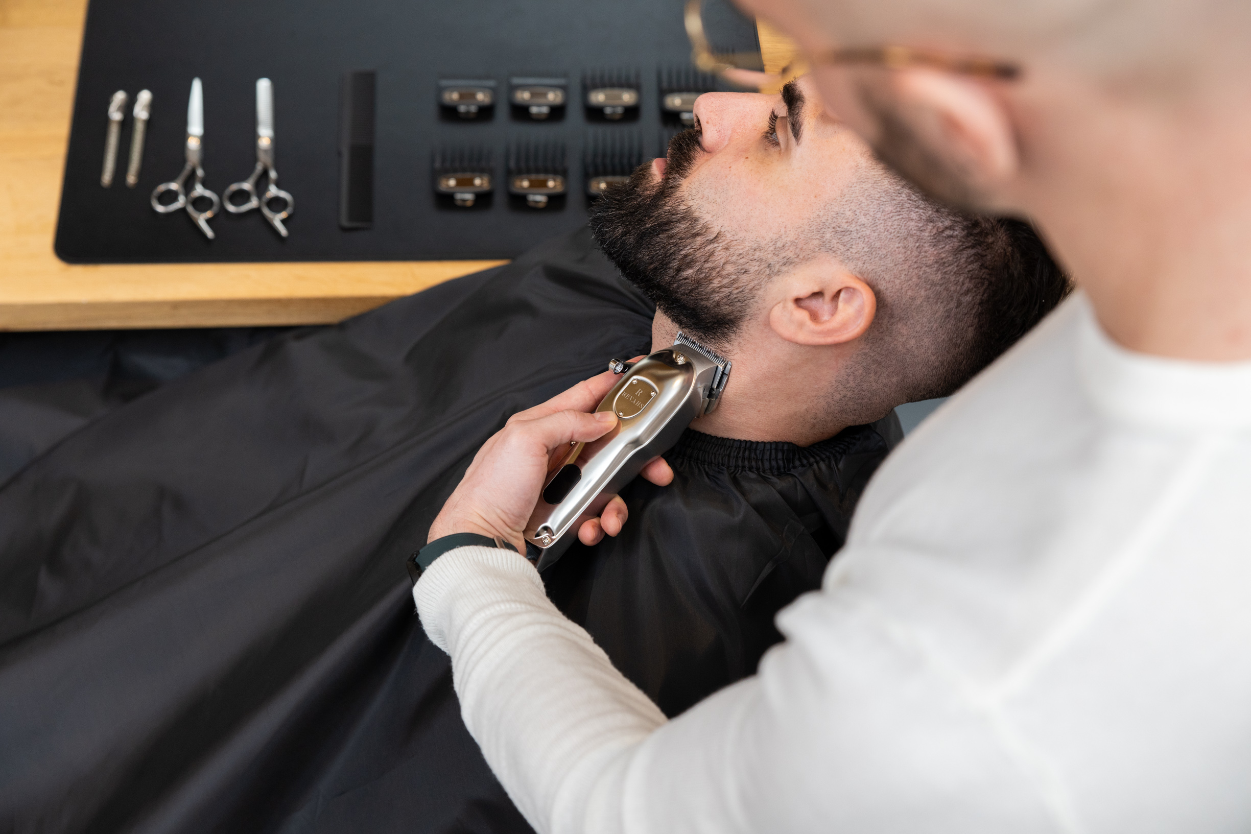 Friseur schneidet Bart eines Mannes mit elektrischem Trimmer in einem Salon.
