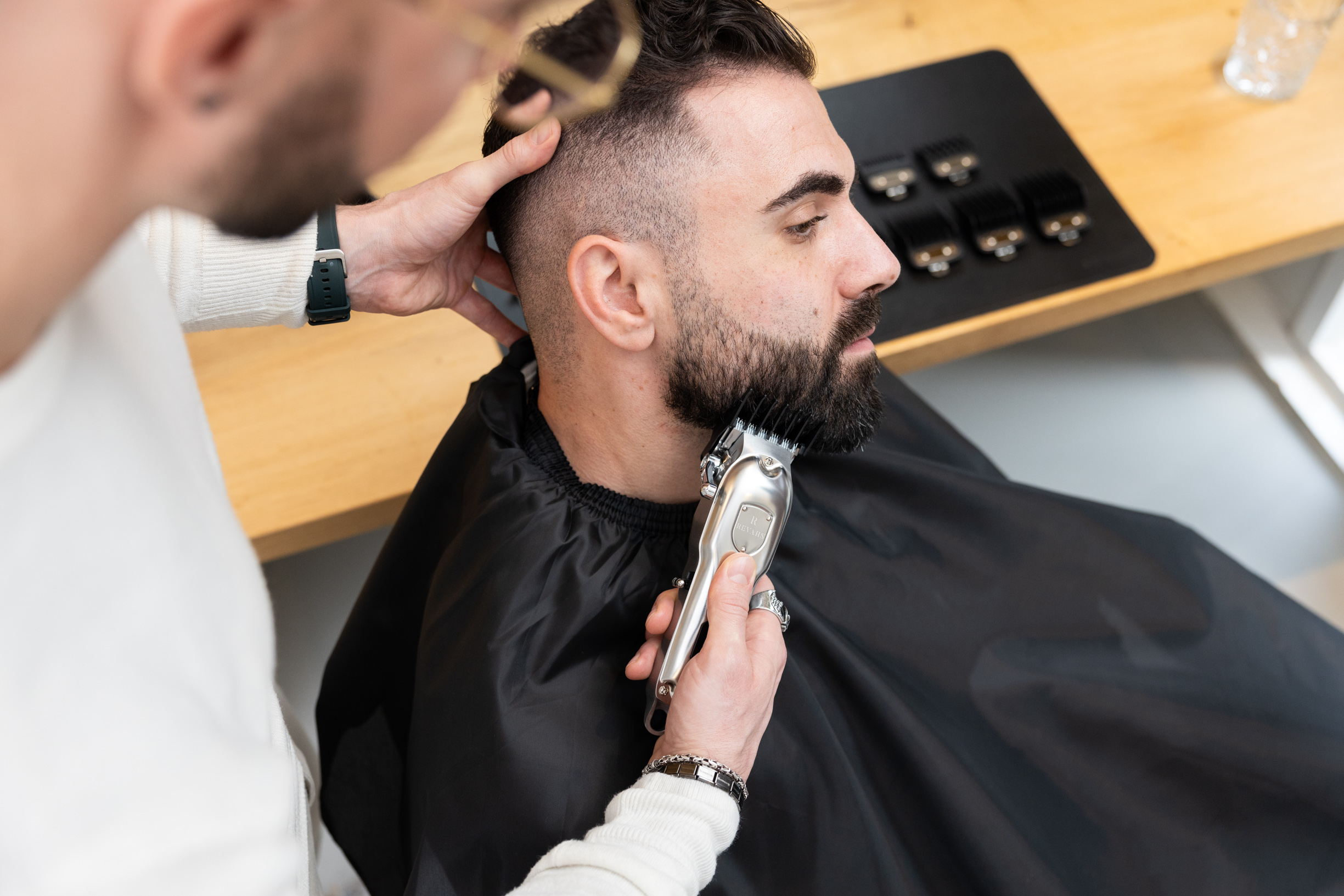 Friseur schneidet Bart eines Mannes mit Trimmer. Nahaufnahme, Fokus auf Friseur und Kunde.