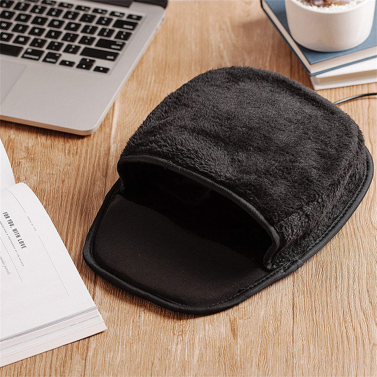Ein schwarzes, flauschiges, beheiztes Mauspad mit einem Laptop und einem Buch auf einem Holzschreibtisch.