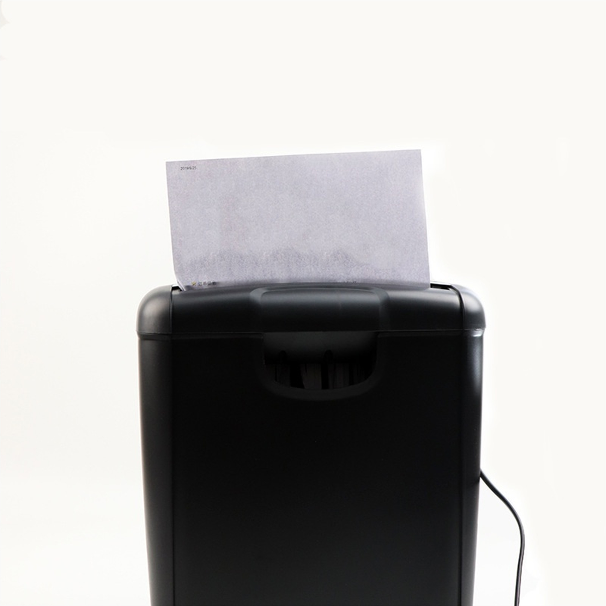 Ein schwarzer Aktenvernichter, in den ein weißes Blatt Papier eingelegt wird. Das Papier hat Text darauf.