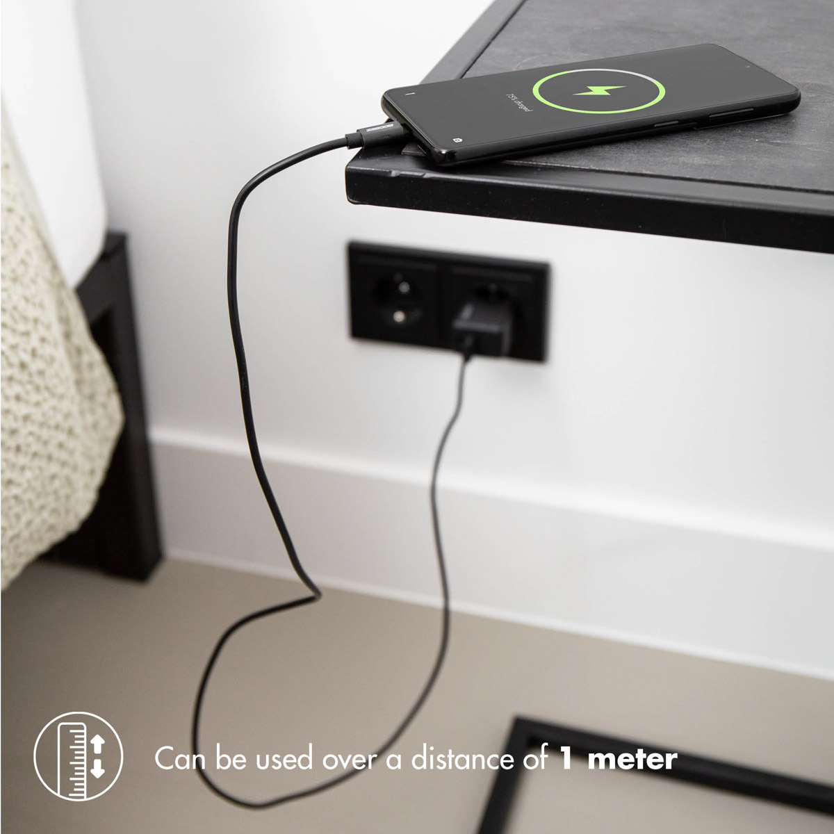 Smartphone noir en charge sur table de nuit. Chargeur dans prise murale, câble noir.