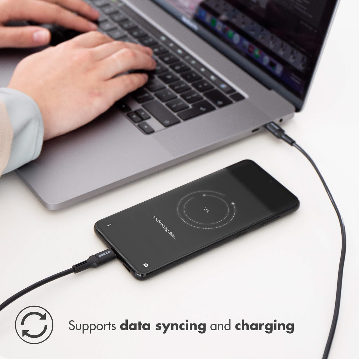 Une main utilise un ordinateur portable, avec un téléphone en charge et synchronisation de données.