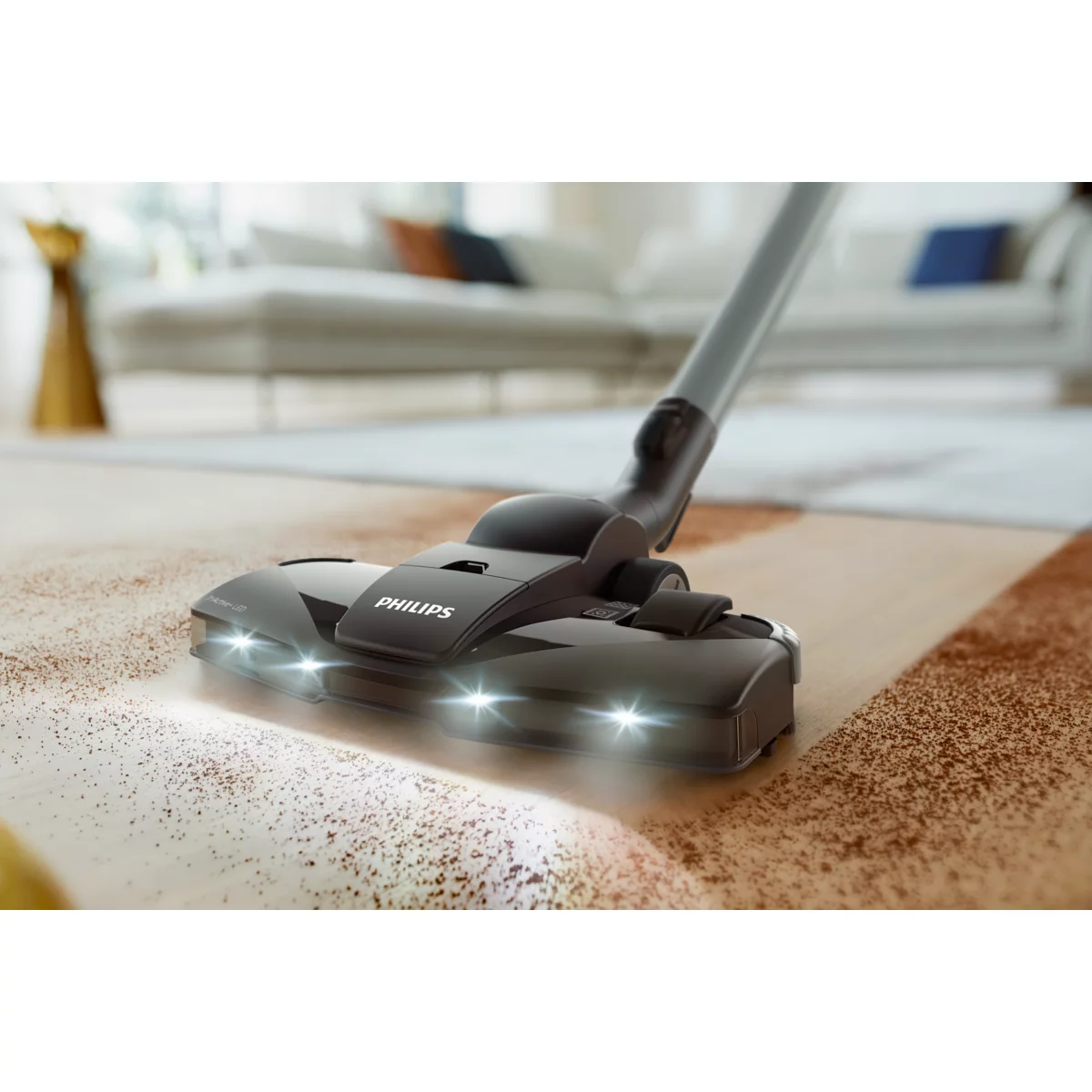 Nahaufnahme eines Staubsaugerkopfes auf einem Teppich. Die Lichter sind an, und etwas Schmutz liegt auf dem Teppich.