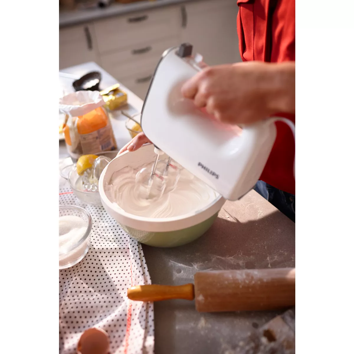 Una persona usa una batidora de mano blanca para batir crema en un bol sobre una mesa.