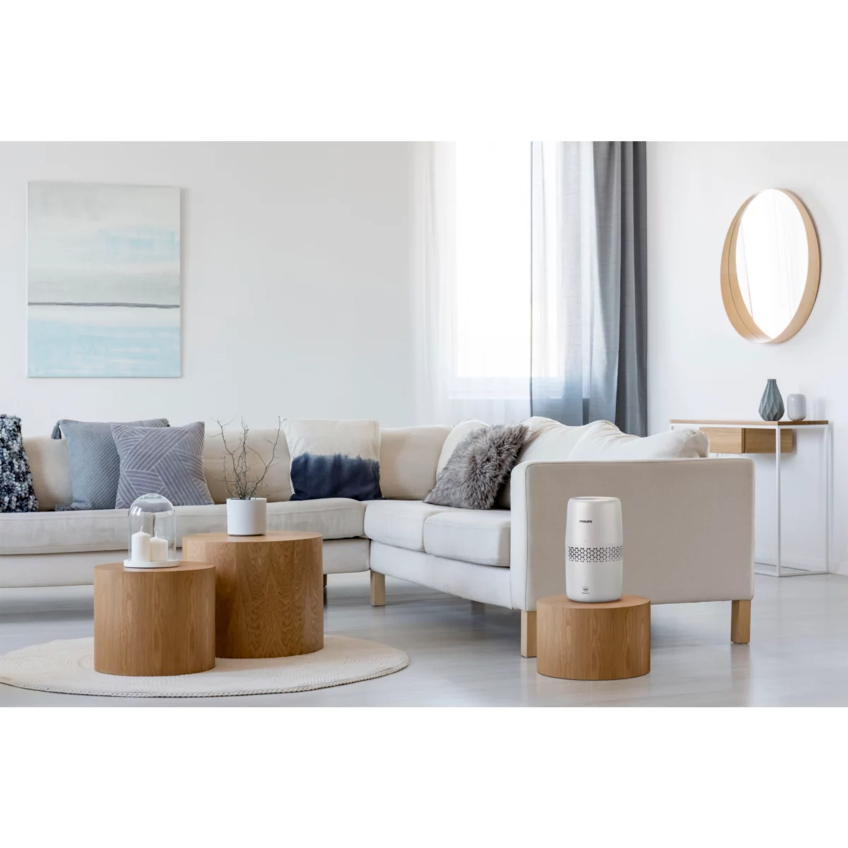 Un salón con un sofá blanco, mesas de madera y un purificador de aire. Hay una pintura y un espejo.