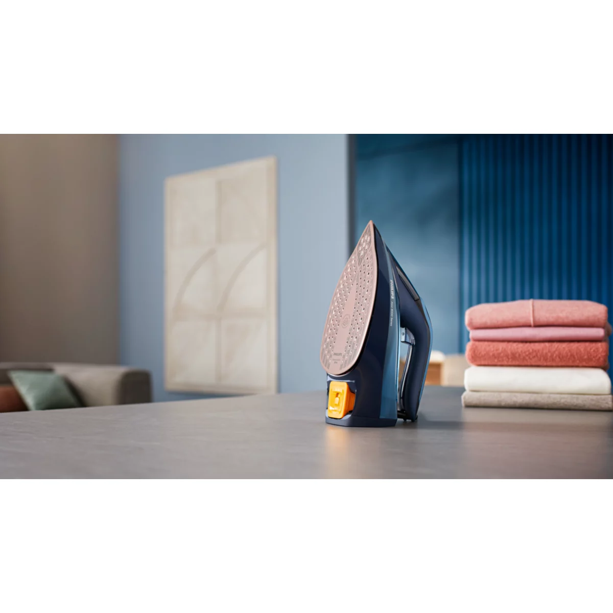 Żelazko na stole obok stosu złożonych ubrań.