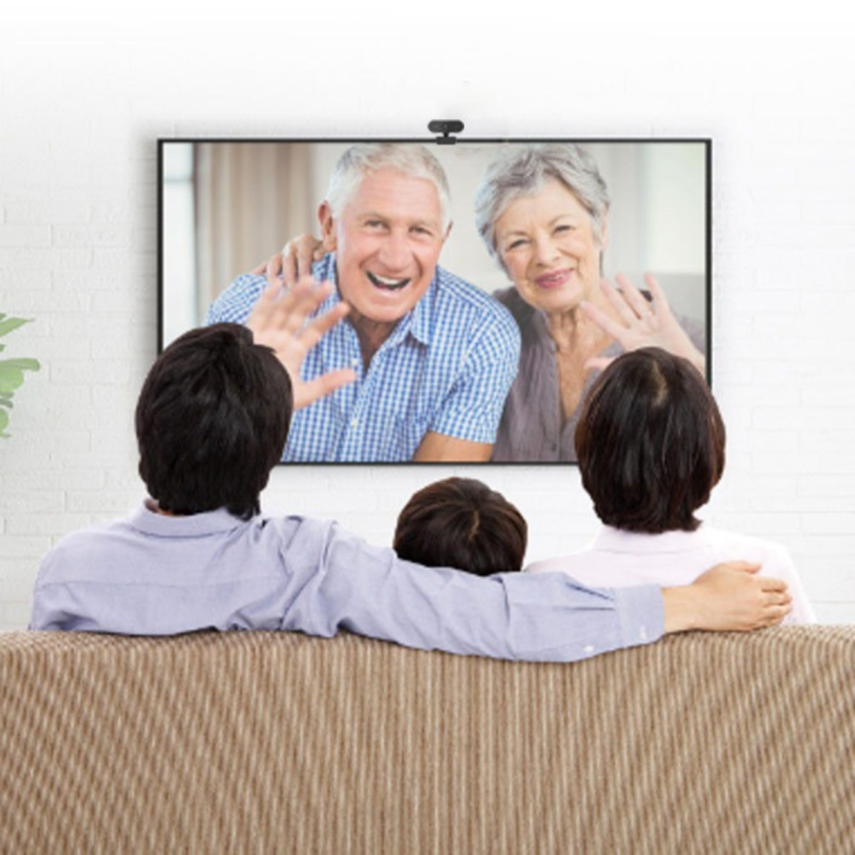 Familie, die einen Videoanruf auf einem Fernseher ansieht, der Bildschirm zeigt ein älteres Ehepaar beim Winken.