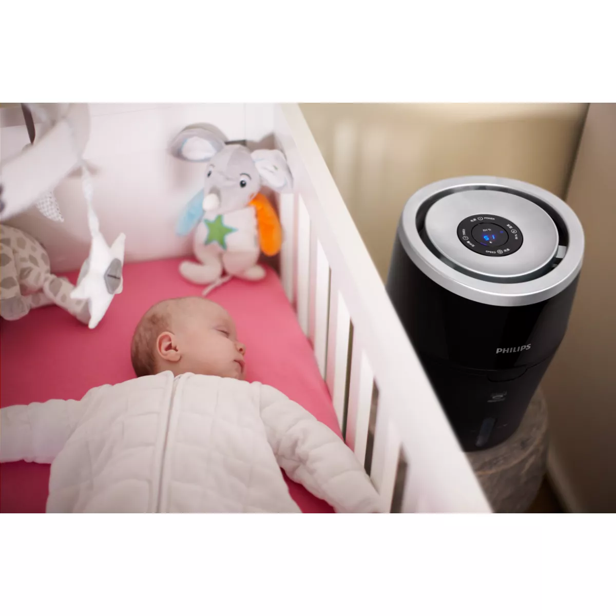 Bambino che dorme in una culla accanto a un purificatore d'aria nero. La stanza ha giocattoli per bambini.