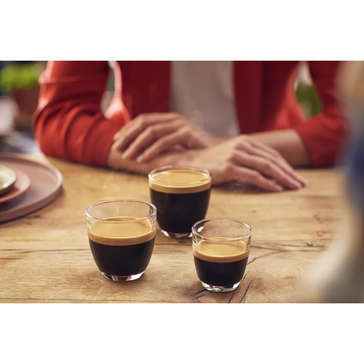 Drei kleine Gläser Espresso auf einem Holztisch. Hände im Hintergrund.
