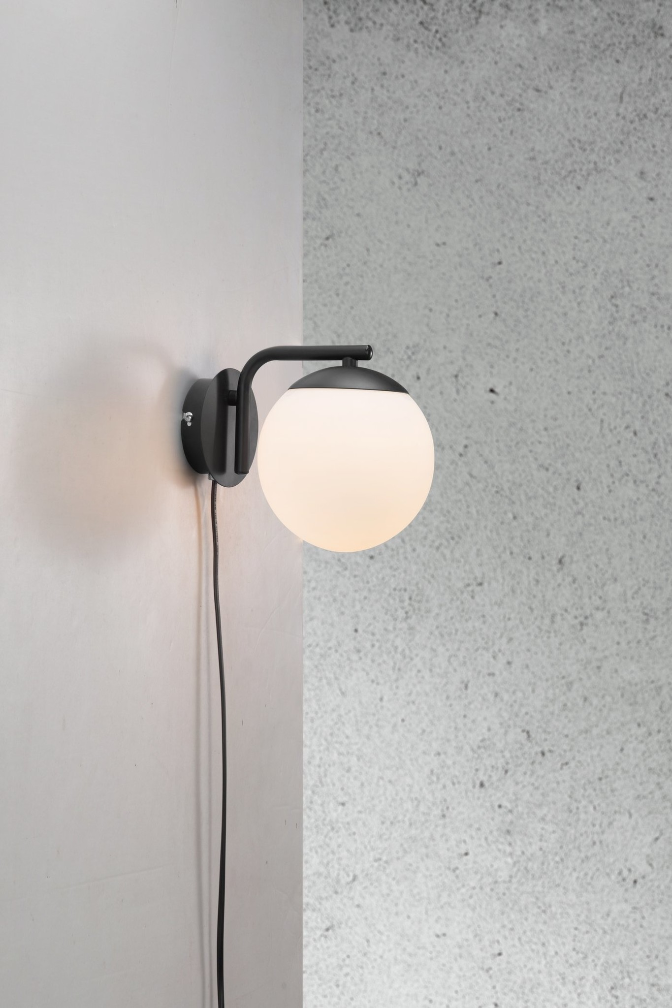 Schwarze Wandleuchte mit weißem Globus. Weiße Wand. Grauer Hintergrund.