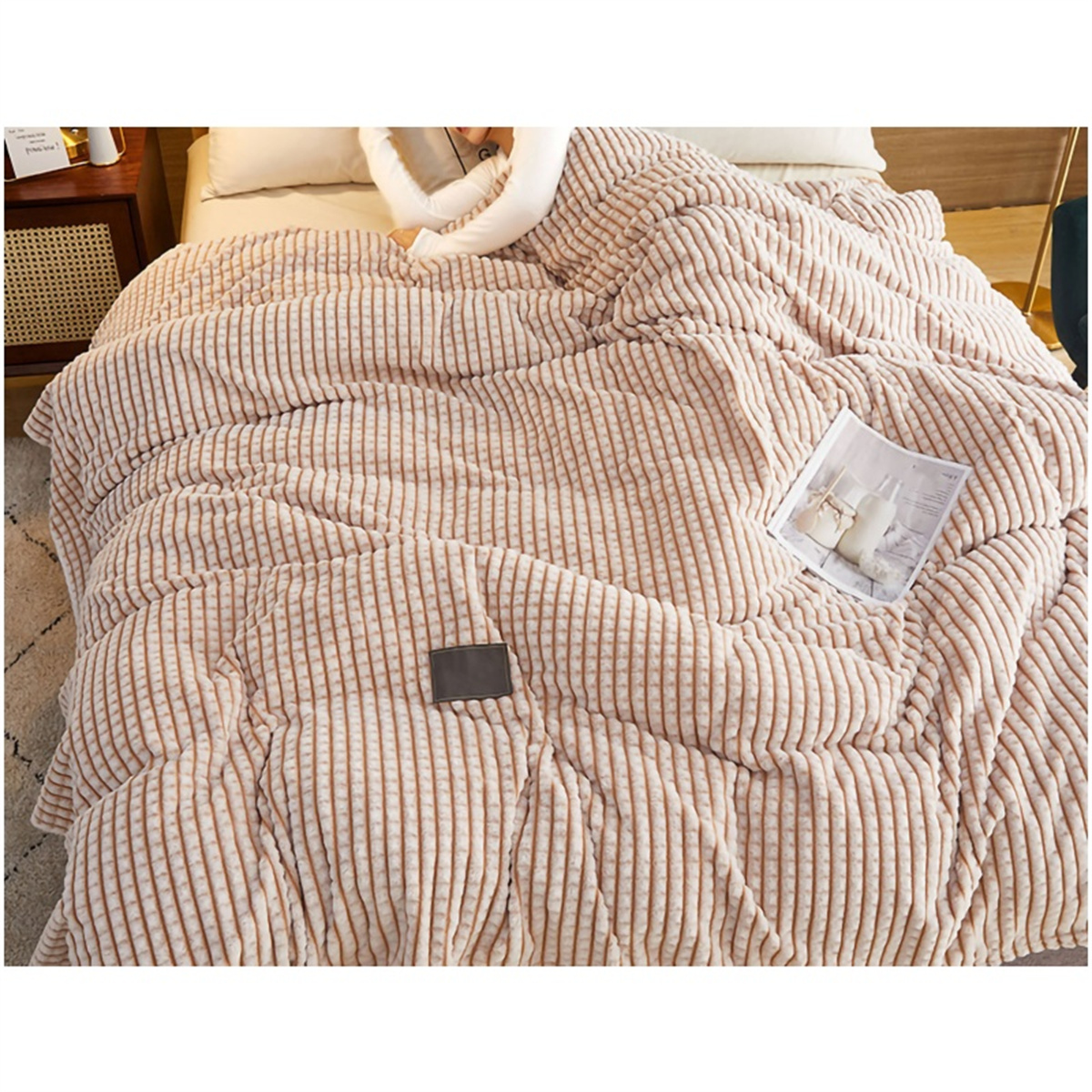Ein gemütliches Bett mit einer gemusterten rosa-beige Decke, einem Kissen und einer Zeitschrift.