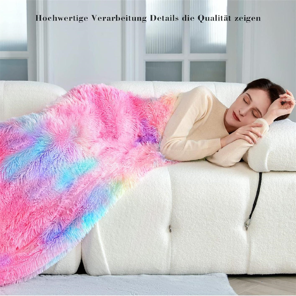 Eine Frau liegt auf einem weißen Sofa, bedeckt von einer flauschigen, bunten Decke. Der Text "Hochwertige Verarbeitung" steht oben.