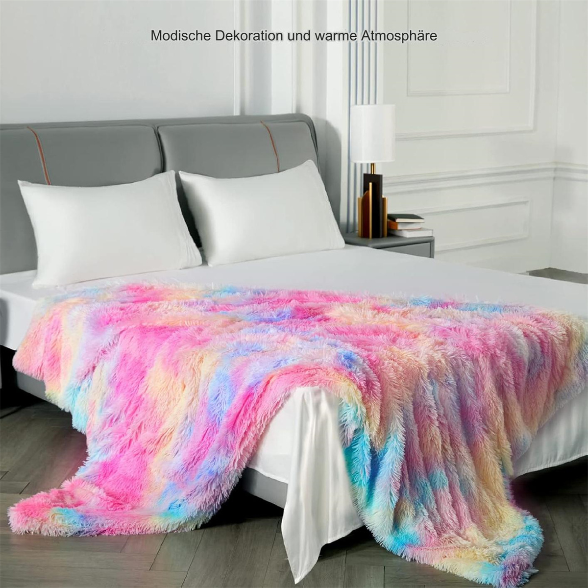 Bett mit einer bunten, flauschigen Decke, weißen Kissen und einer Lampe.