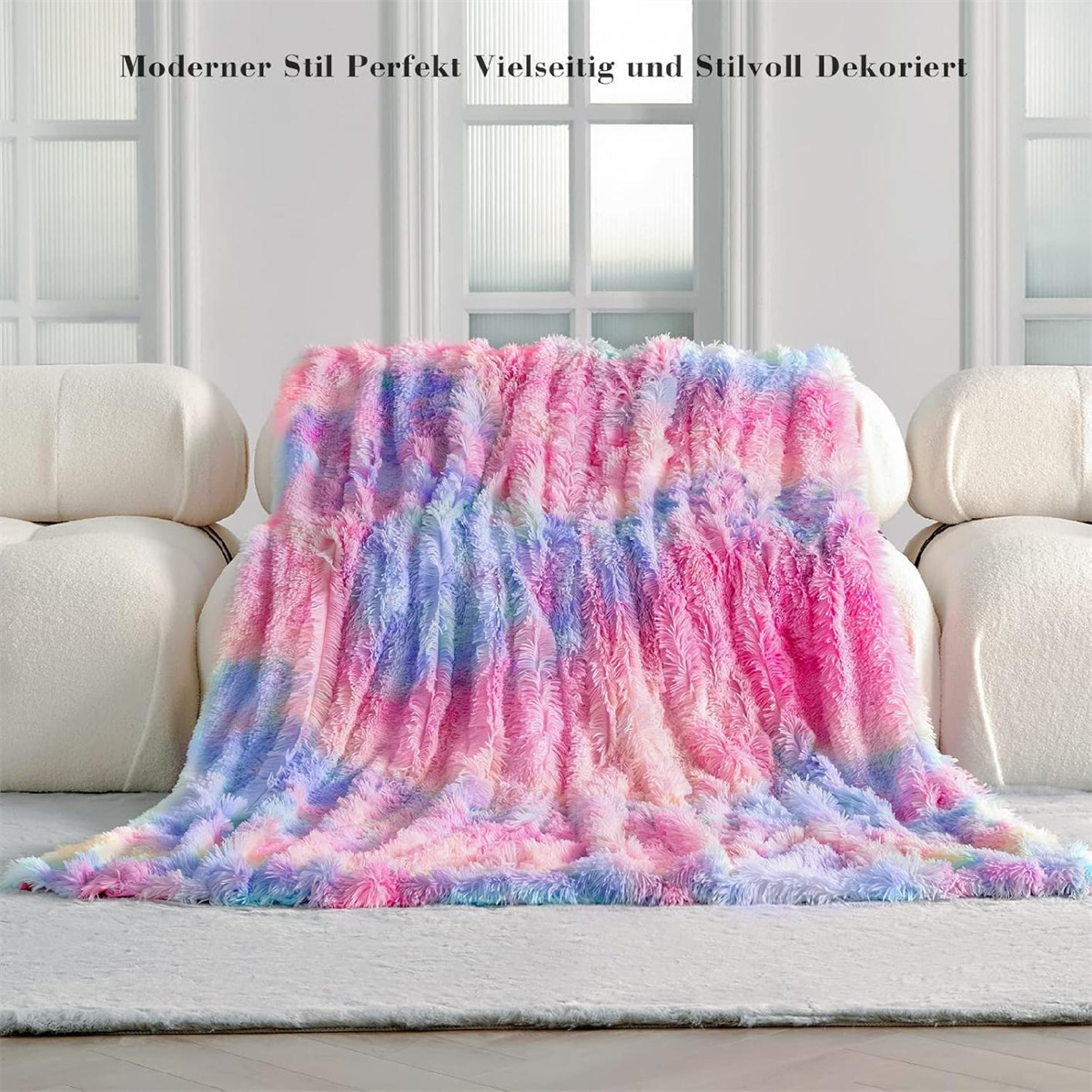 Eine bunte, flauschige Decke auf einer weißen Couch. Die Decke hat rosa, blaue und gelbe Töne.