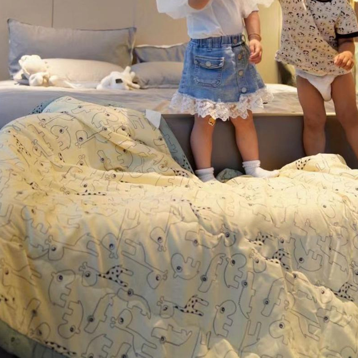 Zwei Kinder stehen auf einem Bett mit gemusterter Decke, mit Stofftier und Kissen, Nahaufnahme der Steppdecke.