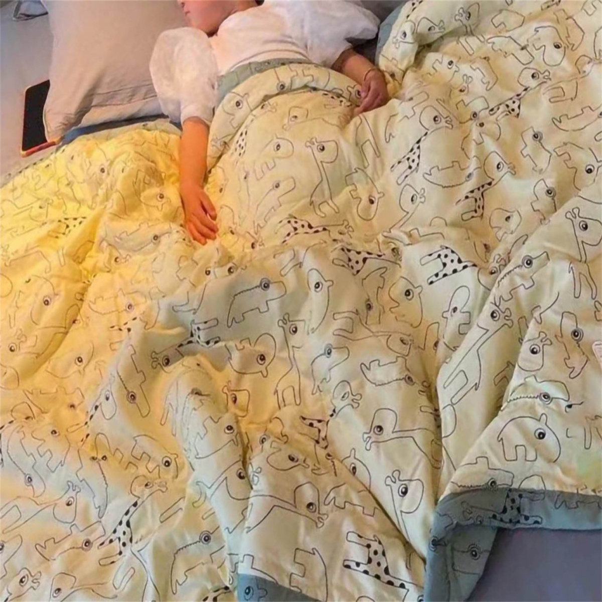 Eine Person liegt im Bett und ist mit einer gemusterten Decke bedeckt. Die Decke hat Tiermuster.