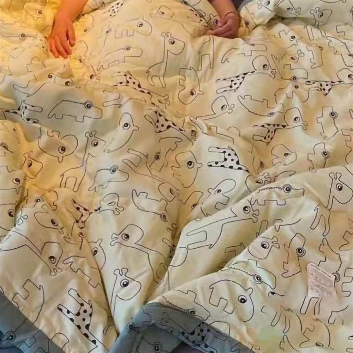 Eine Person unter einer Decke mit Cartoon-Tiermuster, Hände sichtbar.